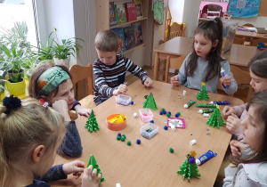 Dzieci ozdabiają papierowe choinki pomponikami akrylowymi i ozdobami